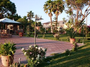 A patio area with outdoor seating, a pergola, and a garden with palm trees and potted plants. - Villa Cristina (Syracuse)