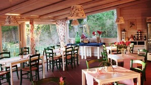 A cozy restaurant with wooden interiors, multiple tables and chairs, and large windows offering a view of greenery outside. - Villa Cristina (Syracuse)