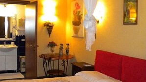 A hotel room with a bed, a bedside table, a mirror, a small table with decorative items, and a wall-mounted light fixture. - Villa Cristina (Syracuse)