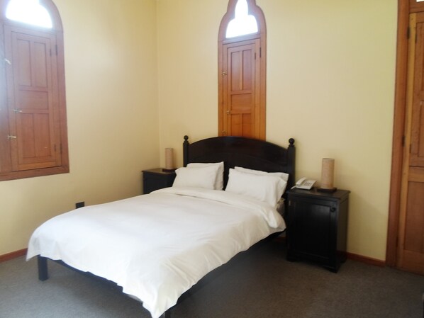 A single bed with white linens in a room with wooden doors and a small bedside table with a lamp. - Posada El Castillo (Arequipa)