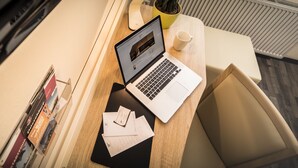 Una computadora portátil sobre un escritorio de madera, con una taza y algunos documentos.