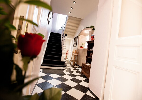 A hallway with a checkered floor, a staircase, and a door on the right.