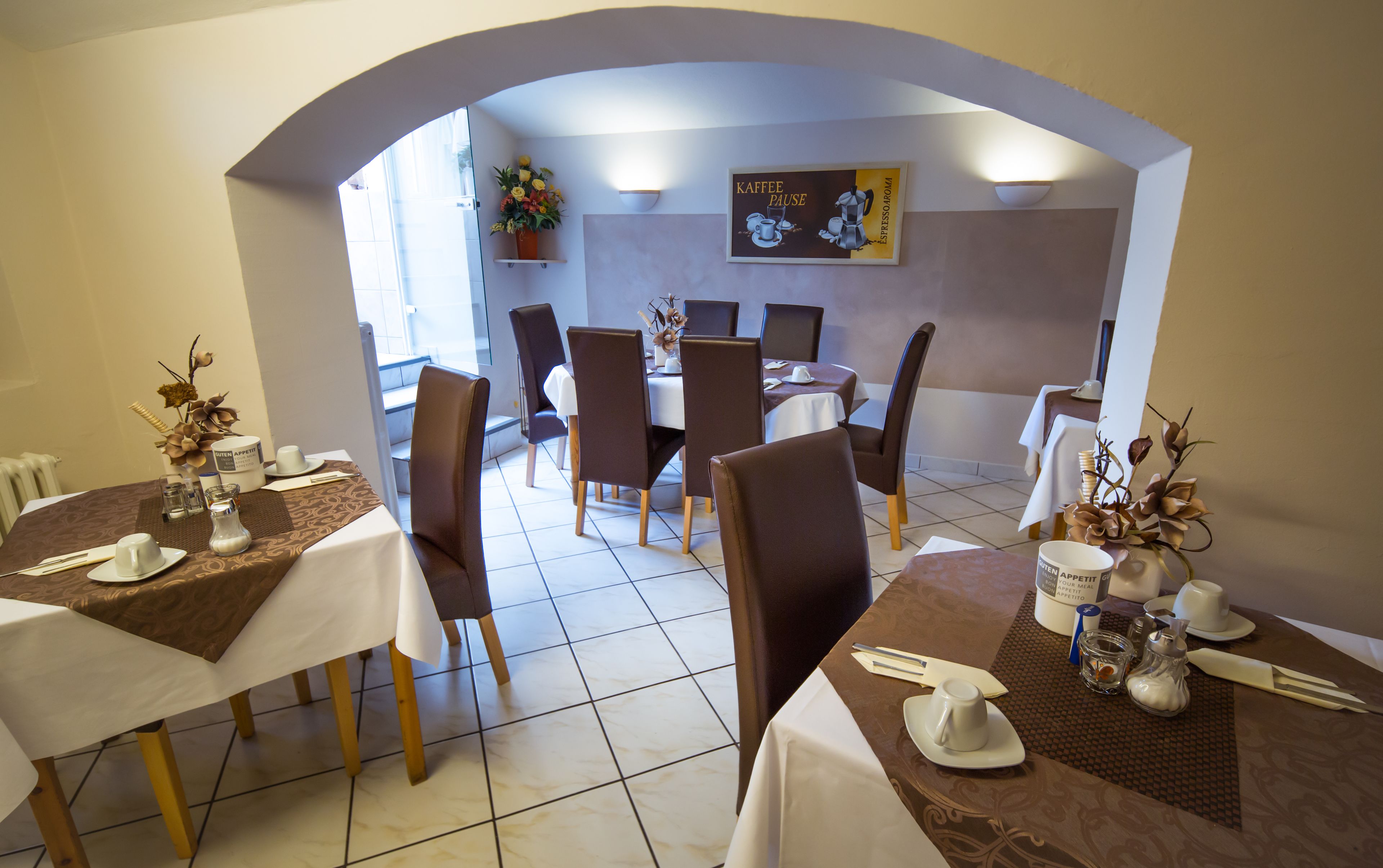 A dining area with tables set for two, chairs, and a wall-mounted sign.