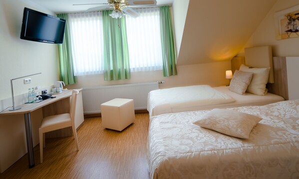 Habitación de hotel con escritorio, dos camas, televisión y ventana con cortinas.