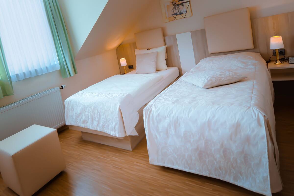 A hotel room with two beds, a small seating area, and a window with curtains.