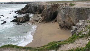 Un paysage côtier caractérisé par des falaises rocheuses, une plage de sable et des vagues qui se brisent sur le rivage.