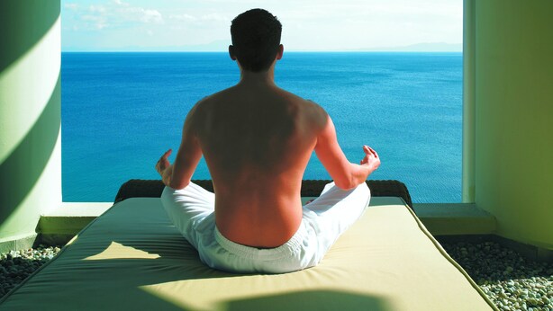 A person meditating on a bed with a view of the sea. - Jaypee Greens Golf & Spa Resort (Greater Noida)