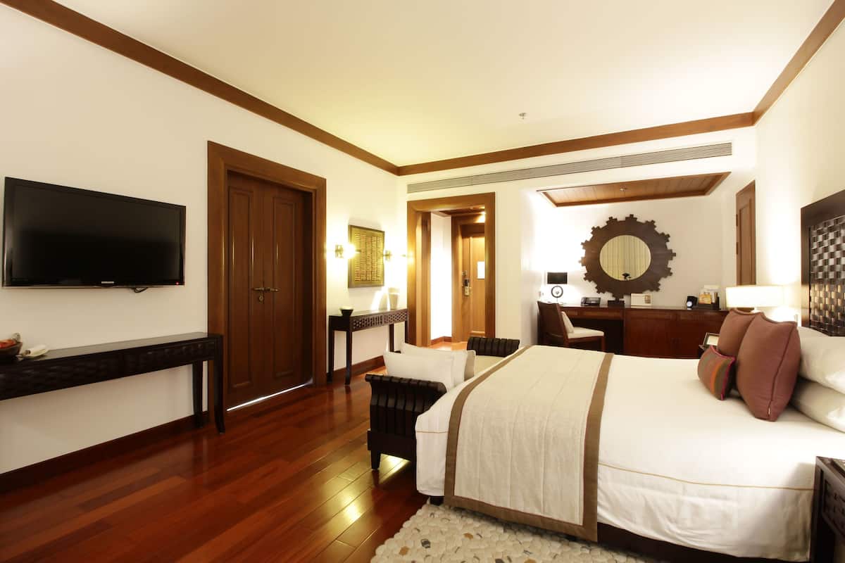 Una habitación de hotel con una cama grande, televisión, piso de madera, escritorio y espejo.