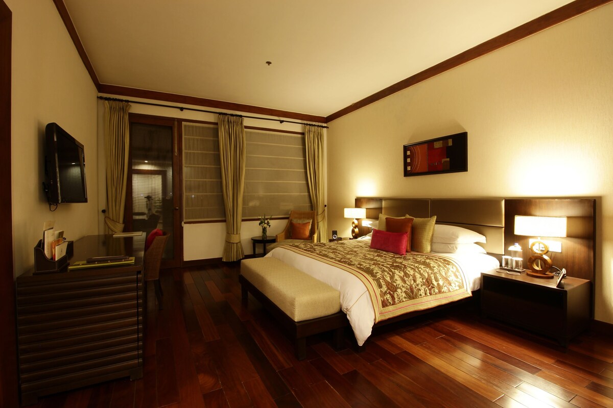 Una habitación de hotel con cama, mesitas de noche, un escritorio con silla, televisor y cortinas.
