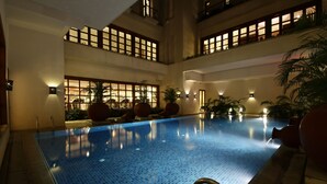 An indoor swimming pool with tiled flooring, multiple levels with balconies, and ambient lighting. - Jaypee Greens Golf & Spa Resort (Greater Noida)