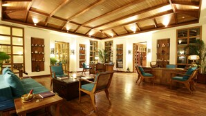 A spacious living area with wooden flooring, a high ceiling with exposed beams, and a variety of seating options including sofas and chairs. - Jaypee Greens Golf & Spa Resort (Greater Noida)