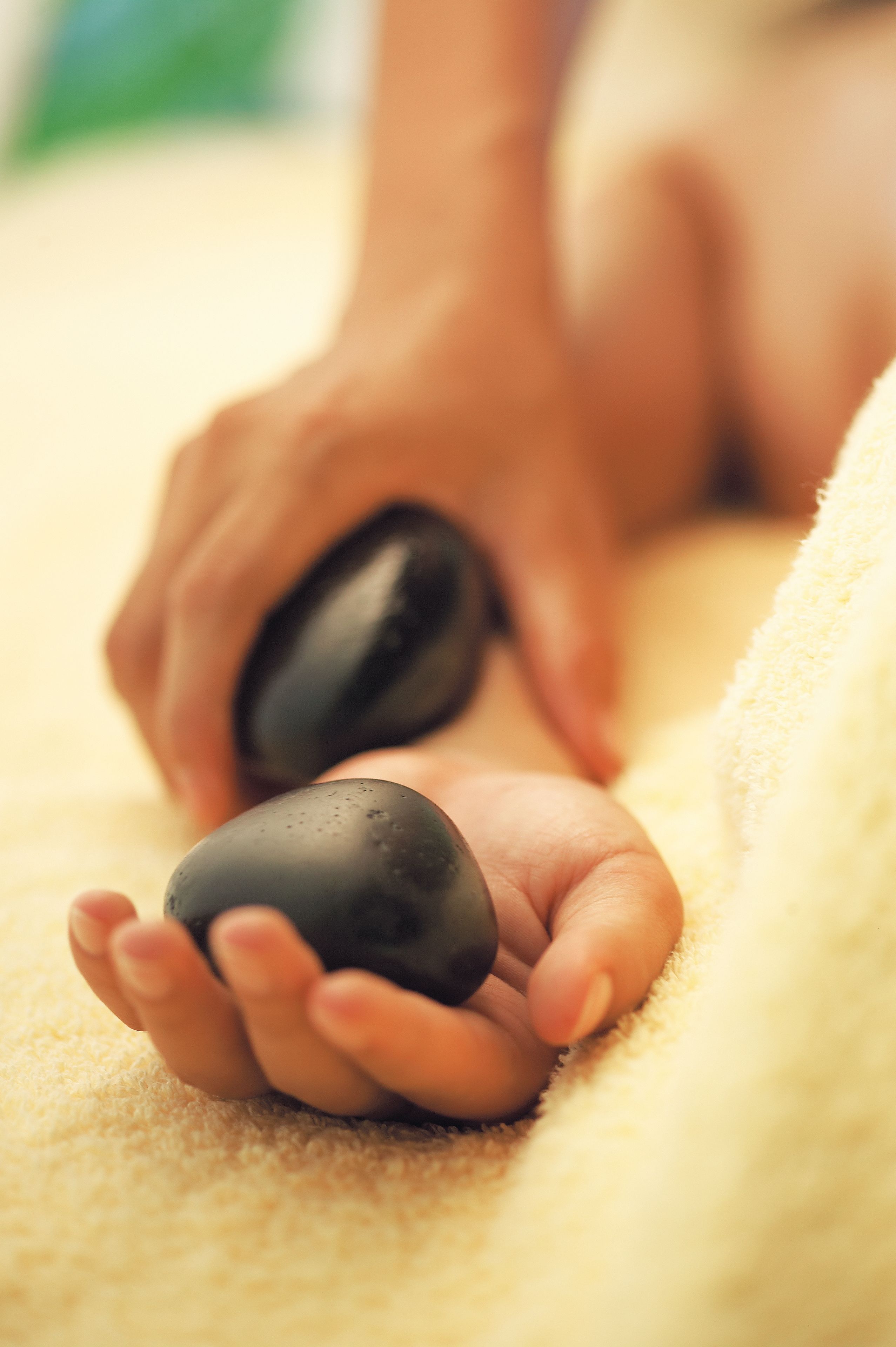 Gros plan sur des mains tenant une pierre noire, probablement utilisée lors d’une séance de massage ou de thérapie.