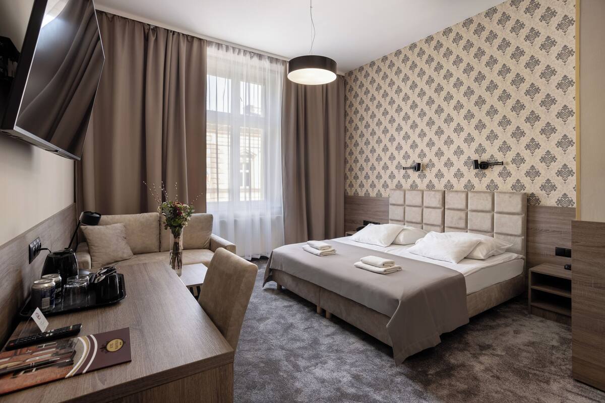 A hotel room with a bed, a desk, a chair, a TV, and a window with curtains.