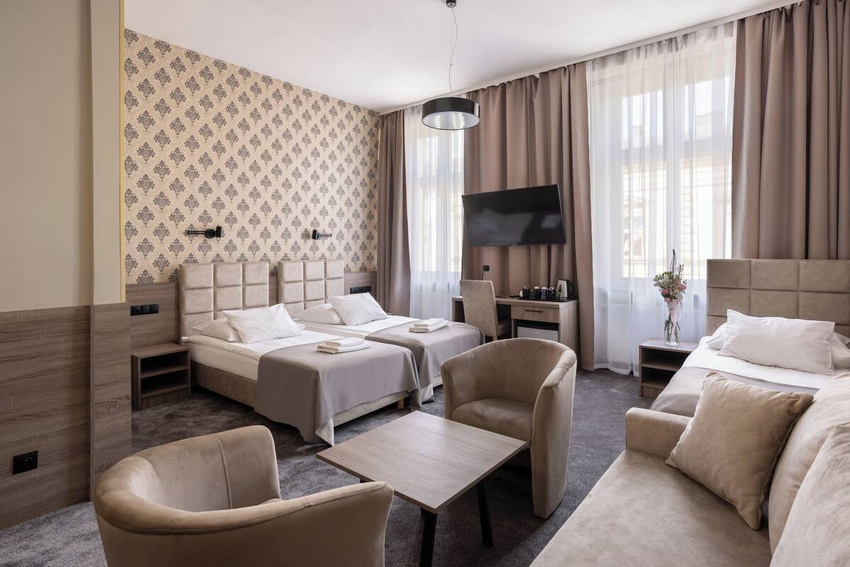 A hotel room with two beds, a desk, a TV, and a seating area.