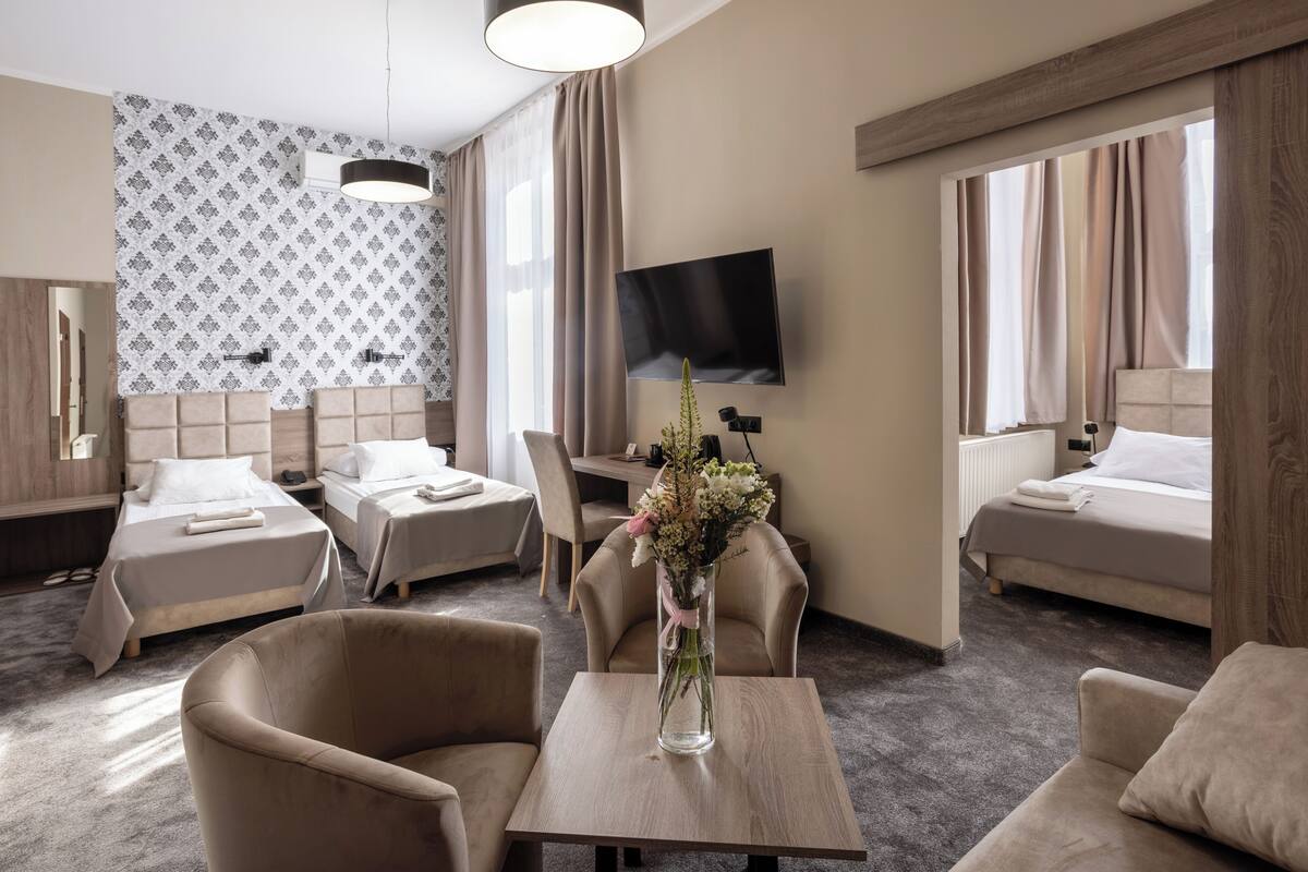 A hotel room with two beds, a TV, a vase with flowers, and a dining area.