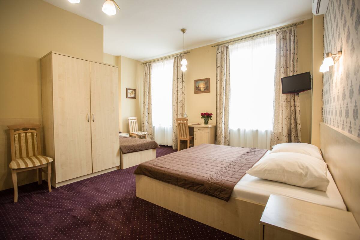 A hotel room with a bed, a desk, a chair, a wardrobe, and a television.