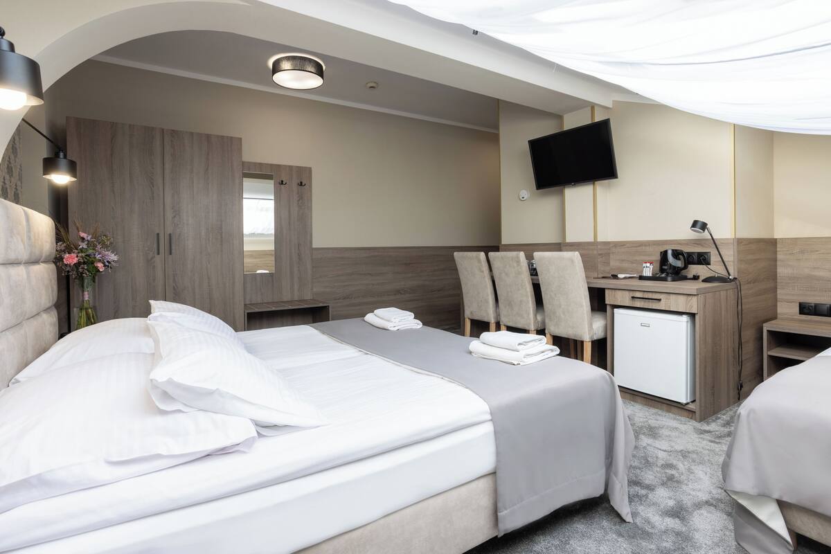 A modern hotel room with a large bed, a desk with a computer, a flat-screen TV, and a small refrigerator.