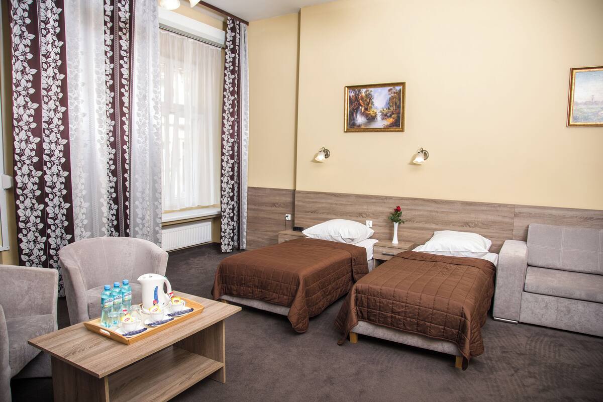 A hotel room with two beds, a sofa, a table with breakfast items, and a painting on the wall.