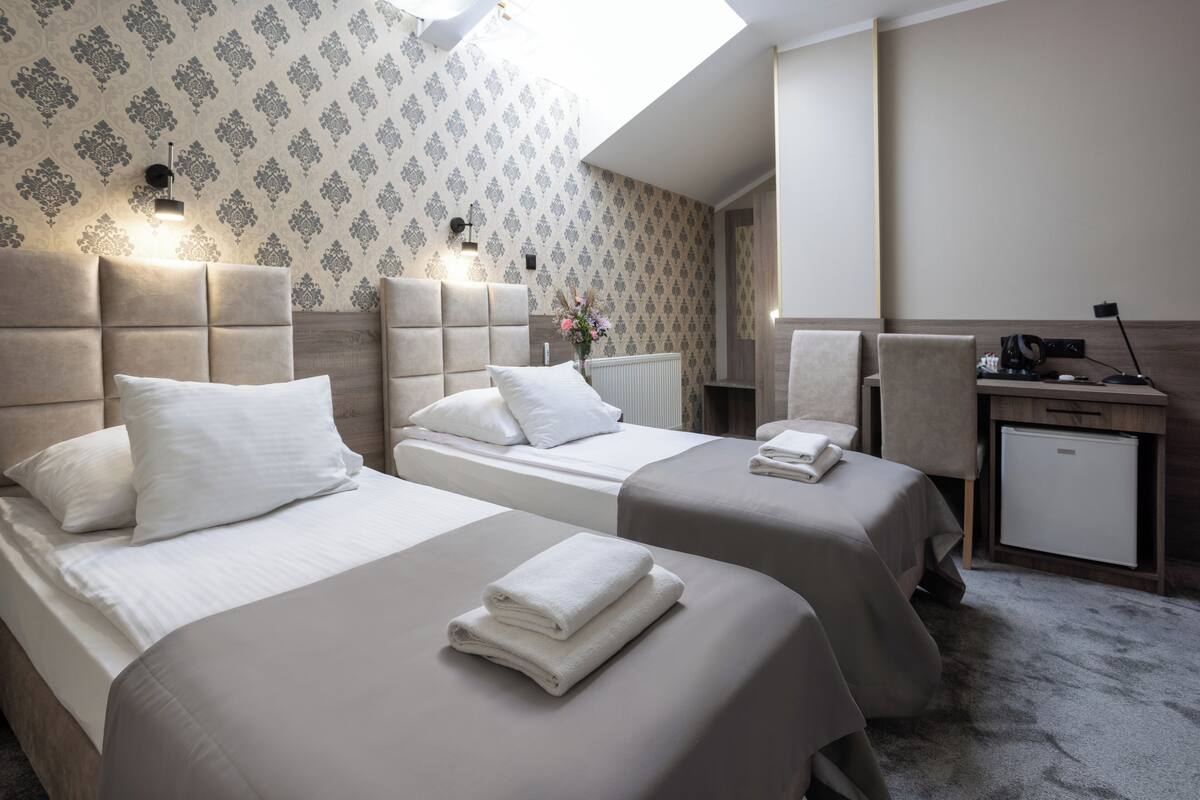 A hotel room with two beds, a desk, a chair, and a small refrigerator.