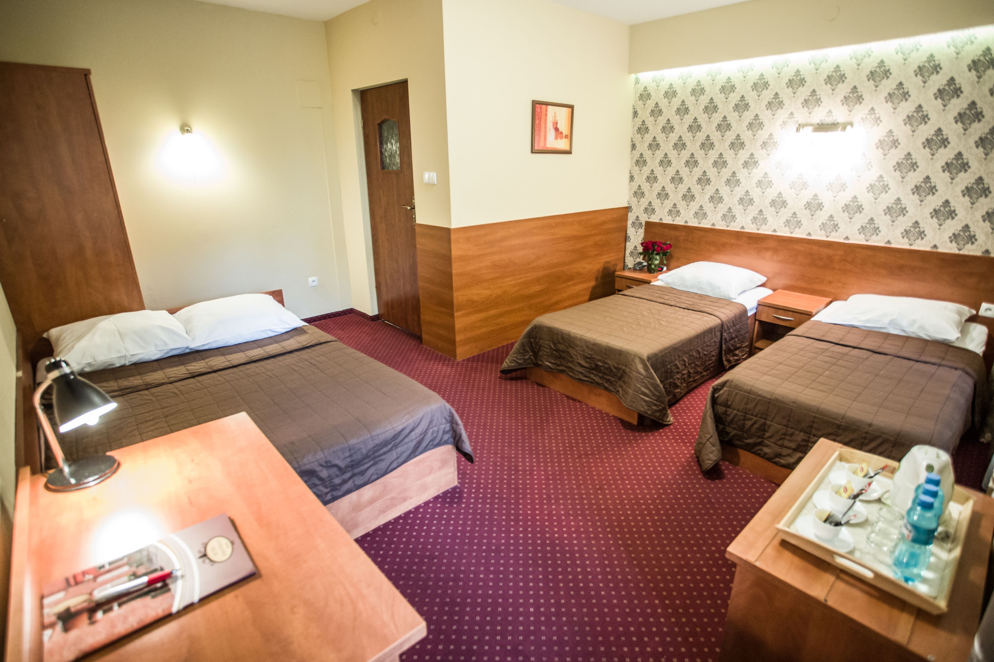 A hotel room with two single beds, a wooden headboard, a desk with a lamp, and a tray with toiletries.