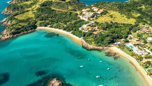 Vista aérea de una zona costera con un mar turquesa transparente, una playa arenosa y un pequeño poblado con casas y una piscina.
