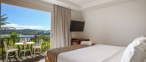 A hotel room with a bed, a TV, a balcony with a table and chairs, and a view of the outdoors.