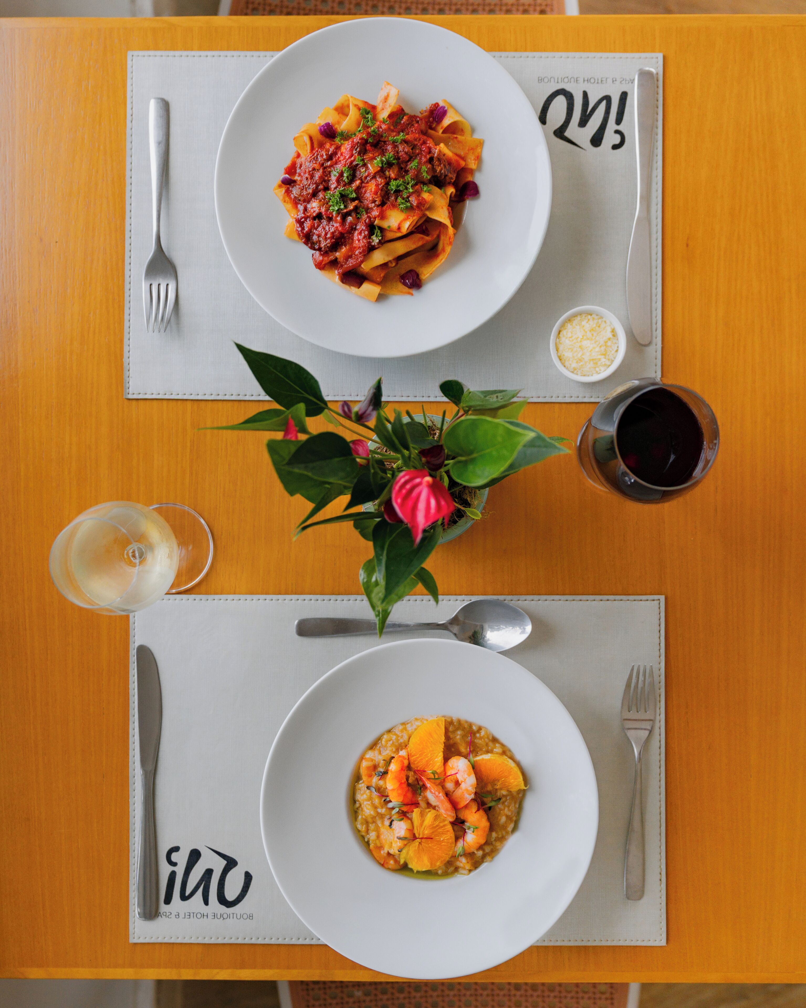 Una mesa con dos platos de pasta y un bol de risotto de mariscos, una copa de vino tinto y una planta pequeña.
