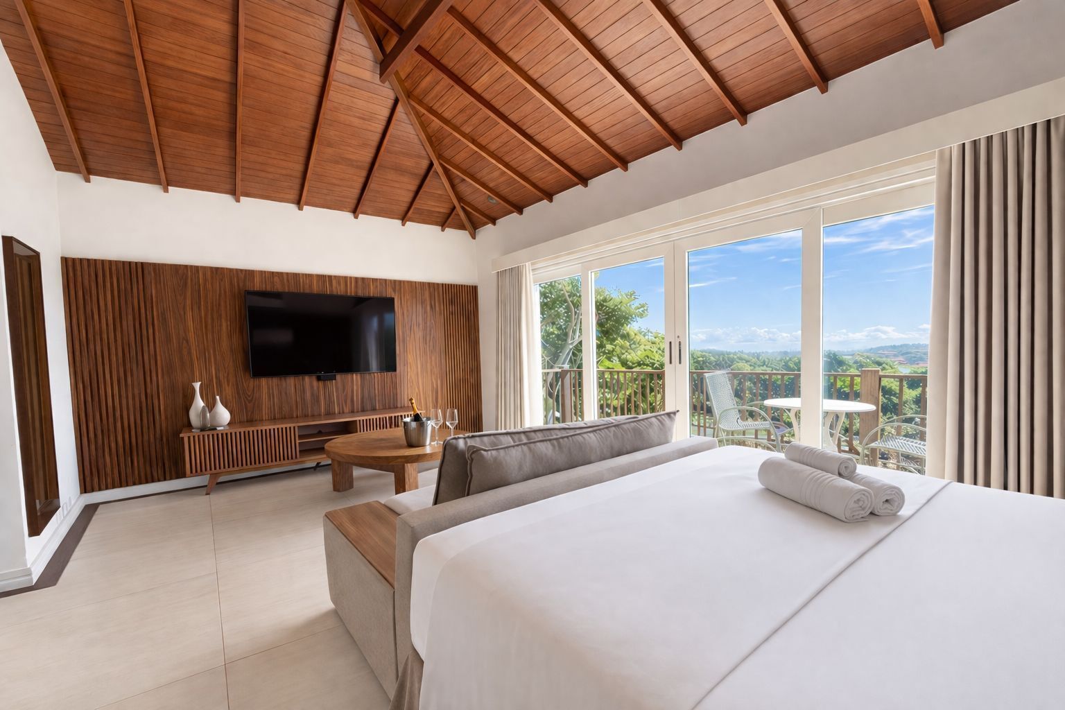 Ein Schlafzimmer mit einem großen Bett, einem Fernseher, einem Balkon mit Tisch und Stühlen sowie einer Holzbalkendecke.