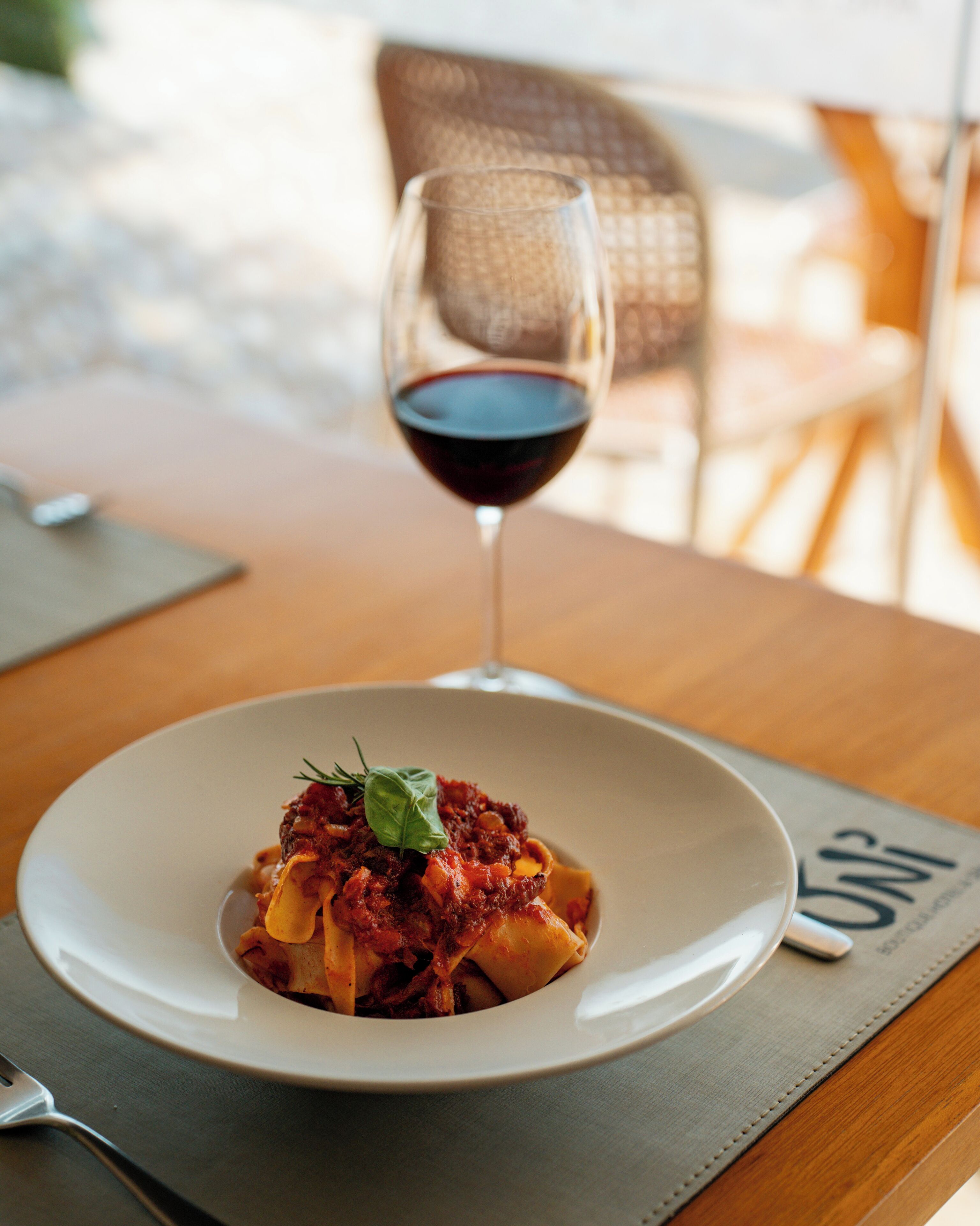 Un plato de pasta con una copa de vino tinto sobre una mesa de madera.