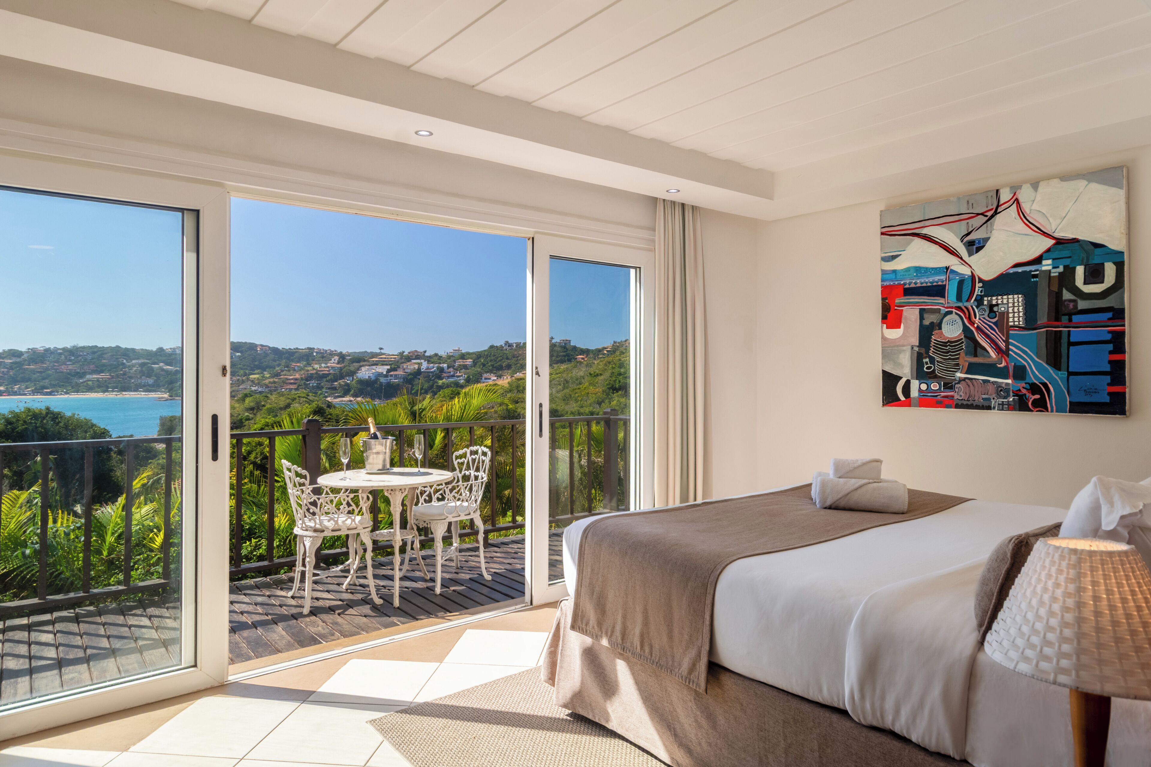 Ein Hotelzimmer mit Balkon, einem Bett, einem Gemälde und Blick auf die Landschaft.