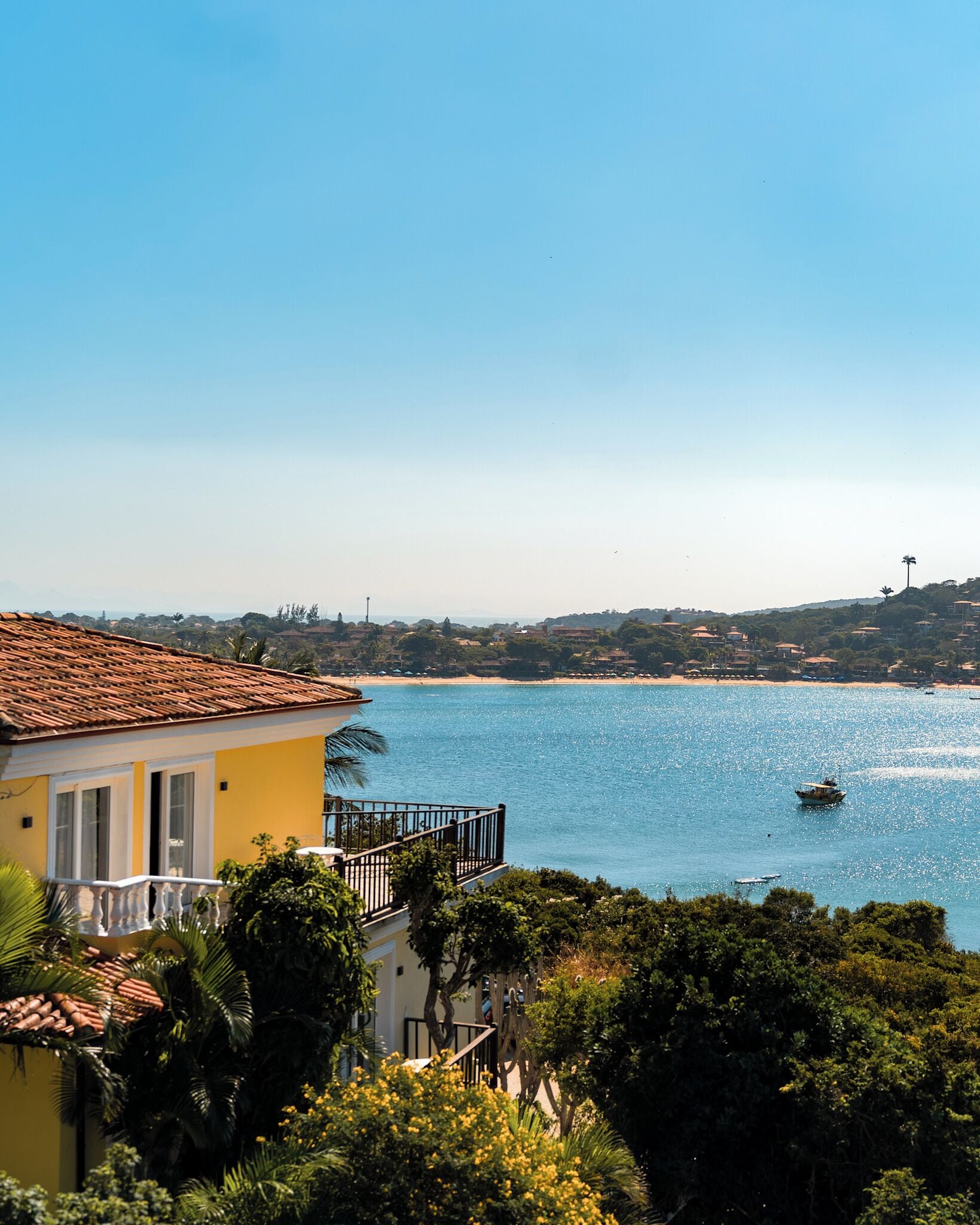 A coastal view with a building featuring a balcony overlooking a clear blue sea.