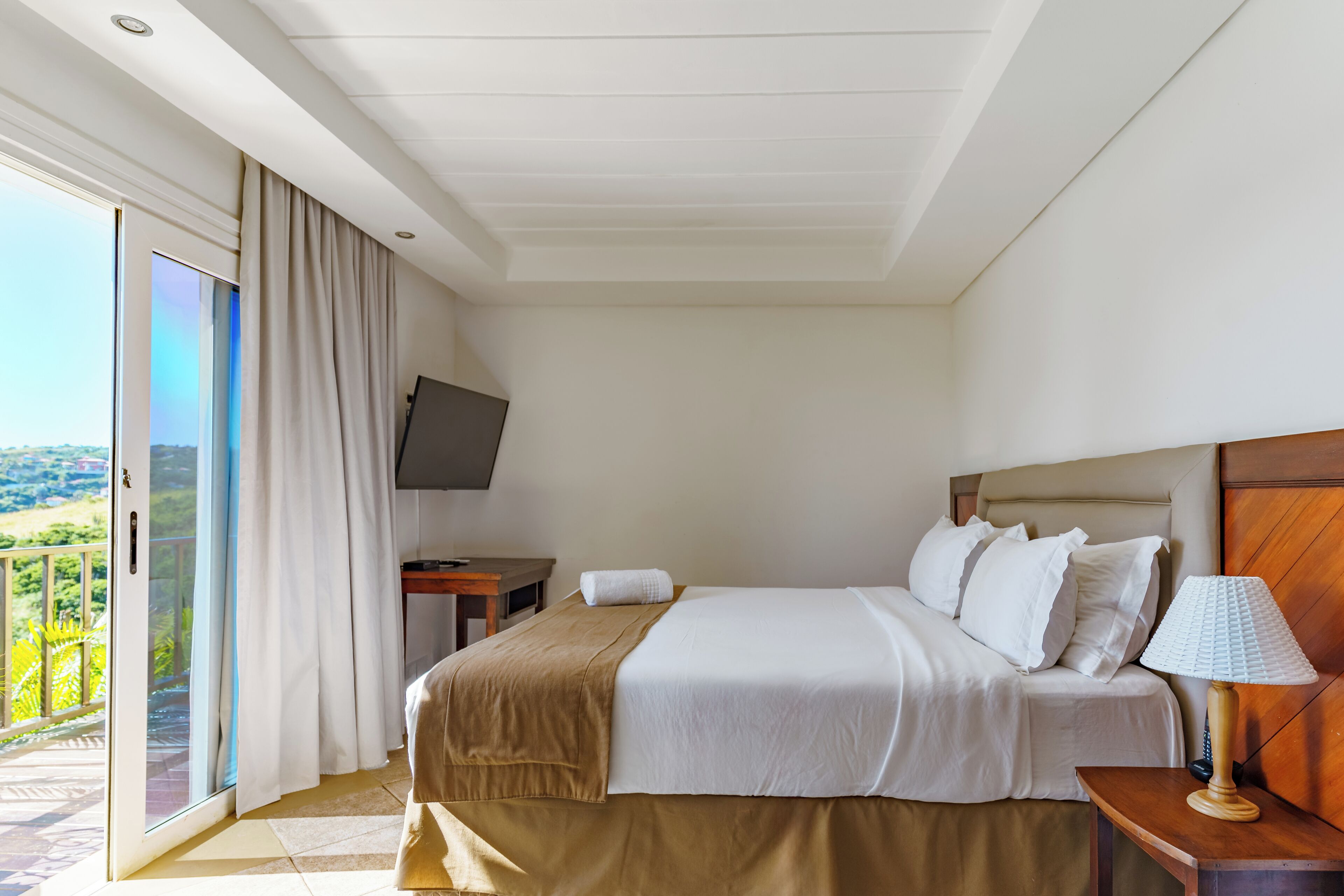 Une chambre d’hôtel avec un lit, un bureau, une télévision et un balcon avec des rideaux.
