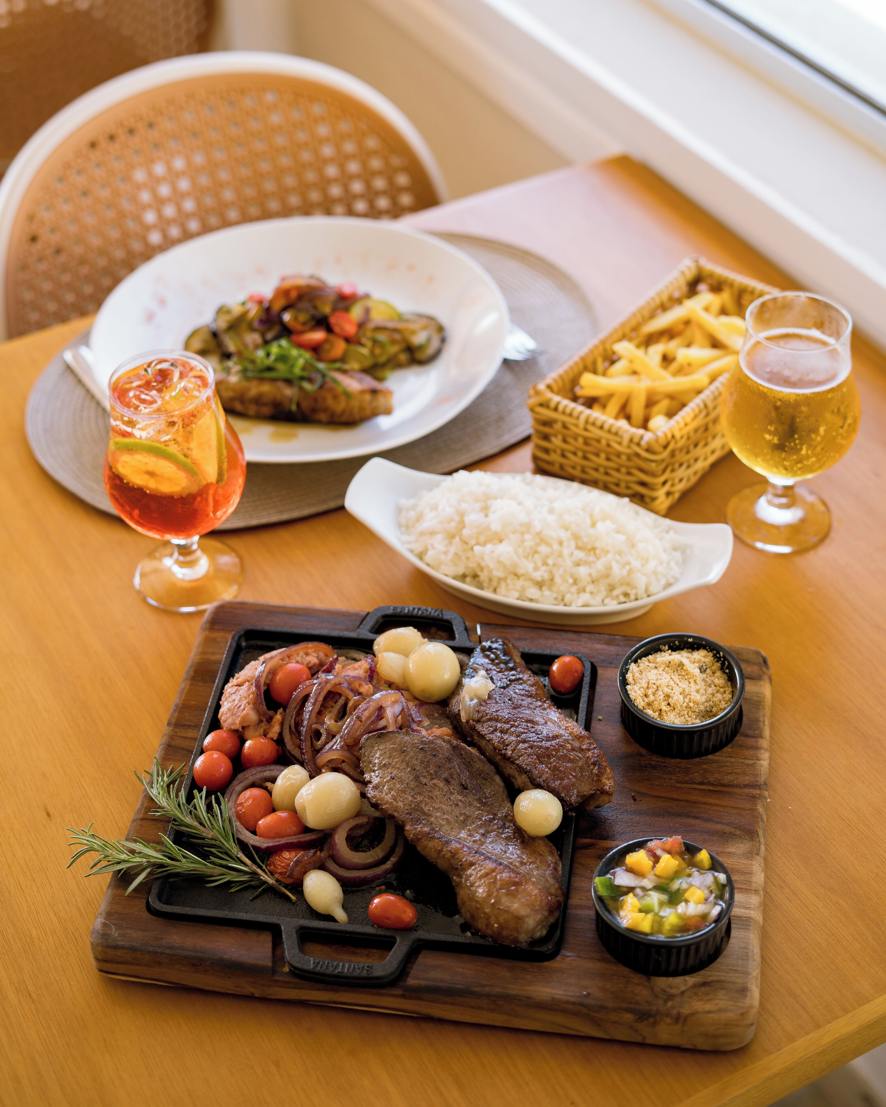 Une table en bois sur laquelle on trouve une variété de plats, notamment un steak, du riz et une salade.