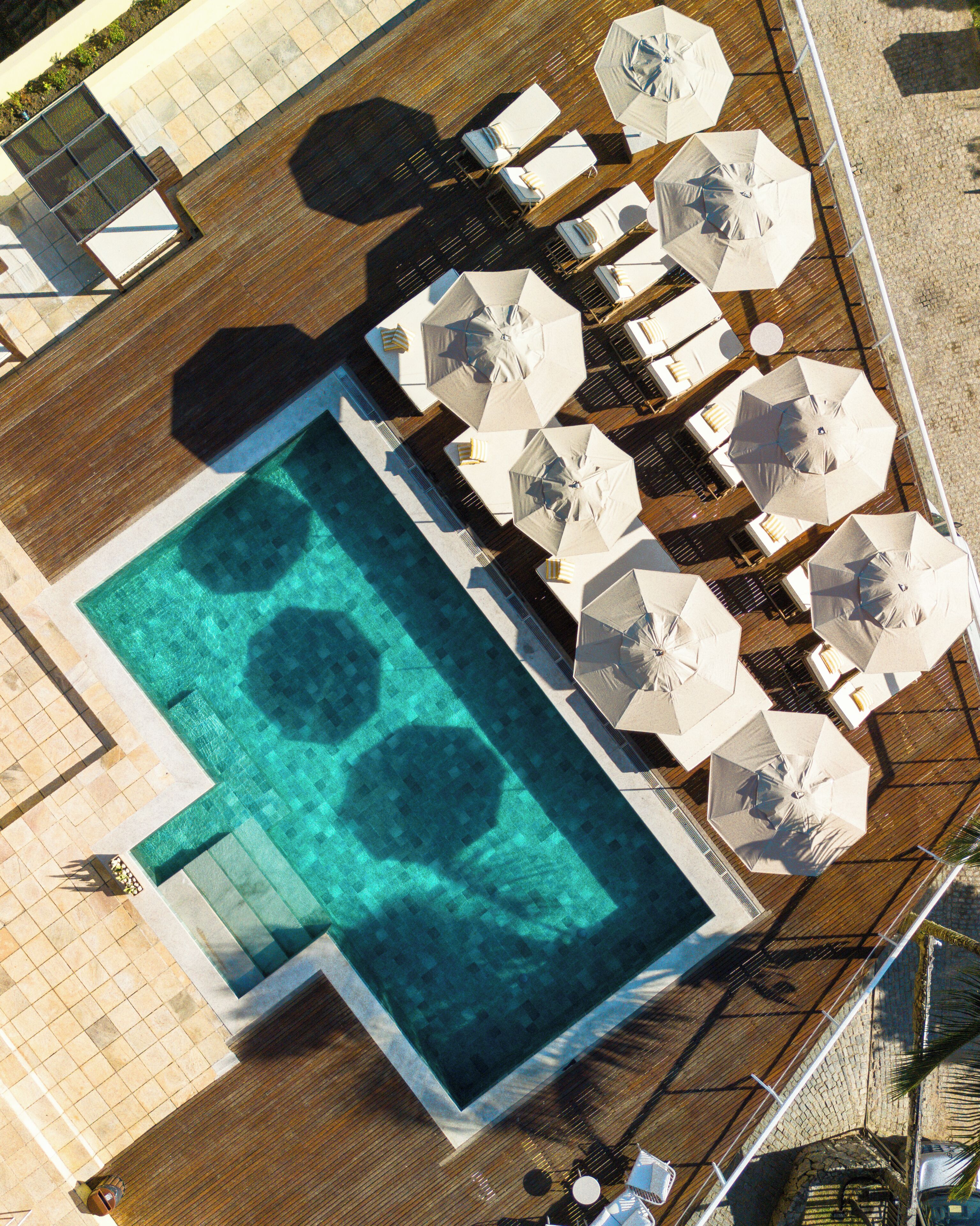 An aerial view of a pool area with a rectangular pool, multiple sun loungers, and umbrellas.