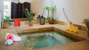 Un moderno espacio de spa con hidromasaje, plantas en macetas, velas y una toalla en el suelo.