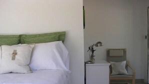 A bedroom with a bed, pillows, a nightstand, a lamp, and a chair. - Cruz Bay Boutique Hotel (St. John)