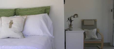 A bedroom with a bed, pillows, a nightstand, a lamp, and a chair.