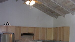 A kitchen with wooden cabinets, a stainless steel refrigerator, a stove, and a microwave. There are two wooden chairs at the island. - Cruz Bay Boutique Hotel (St. John)