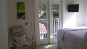 A bedroom with a bed, a chair, a desk lamp, and a door leading to an outdoor area. - Cruz Bay Boutique Hotel (St. John)