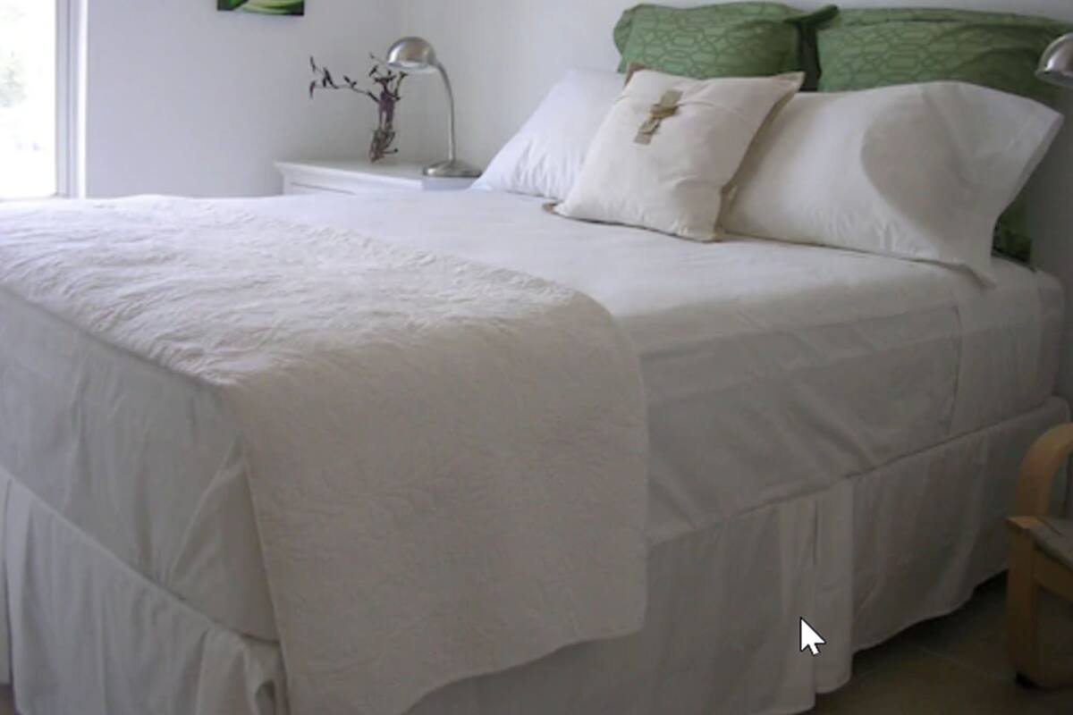 A neatly made bed with white bedding, a green pillow, and a white pillow with a cross design.