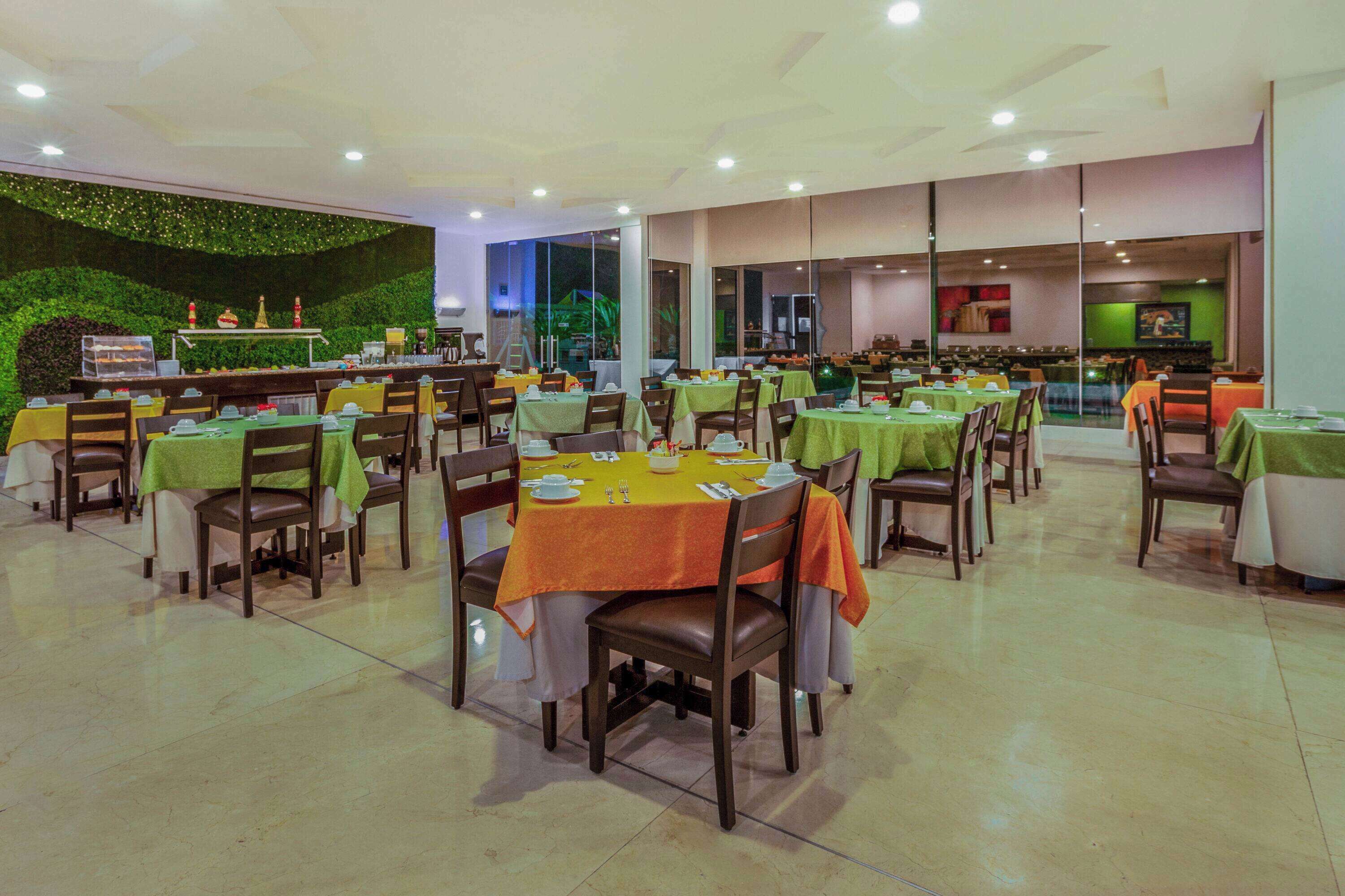 Un restaurant spacieux, doté de nombreuses tables et chaises, d’un mur végétal et offrant une vue sur l’extérieur.