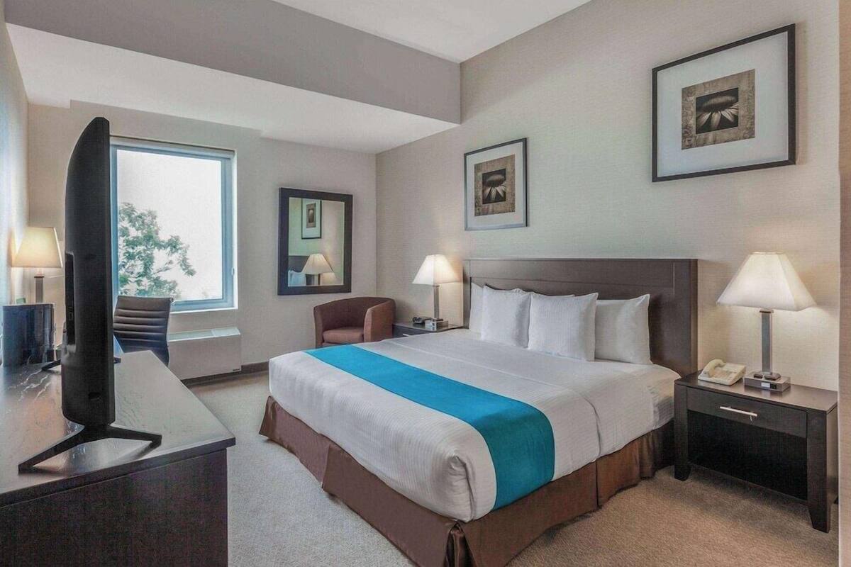 Ett hotellrum med en säng, sängbord, ett skrivbord, en stol och en tv.