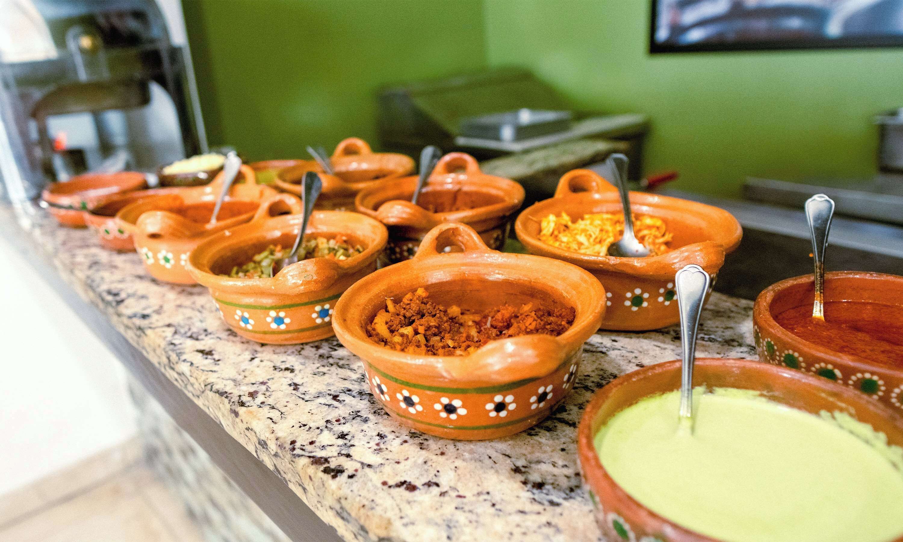 A buffet with various dishes in terracotta bowls, some with spoons.