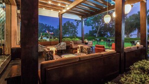 An outdoor seating area with wooden pergola, cushioned seating, and hanging lights.