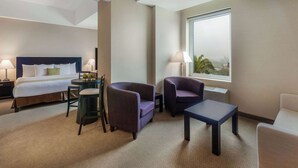 A hotel room with a bed, two armchairs, a small table, and a window with a view.