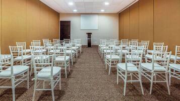 A conference room with rows of white chairs, a carpeted floor, and a large screen at the front.
