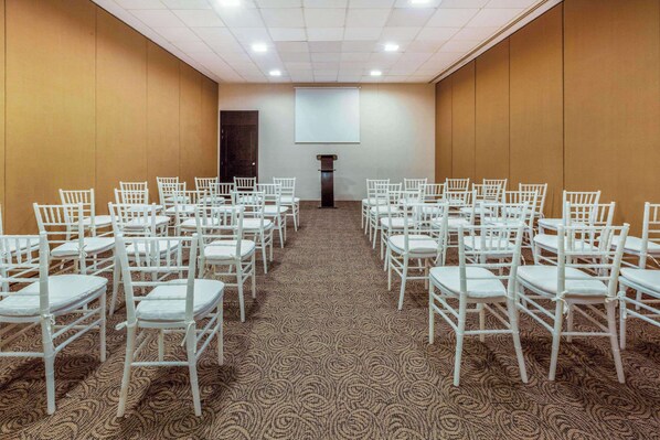 A conference room with rows of white chairs, a carpeted floor, and a large screen at the front.