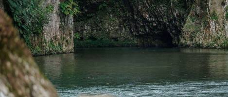 Entrada natural a una cueva con un río tranquilo que la atraviesa.