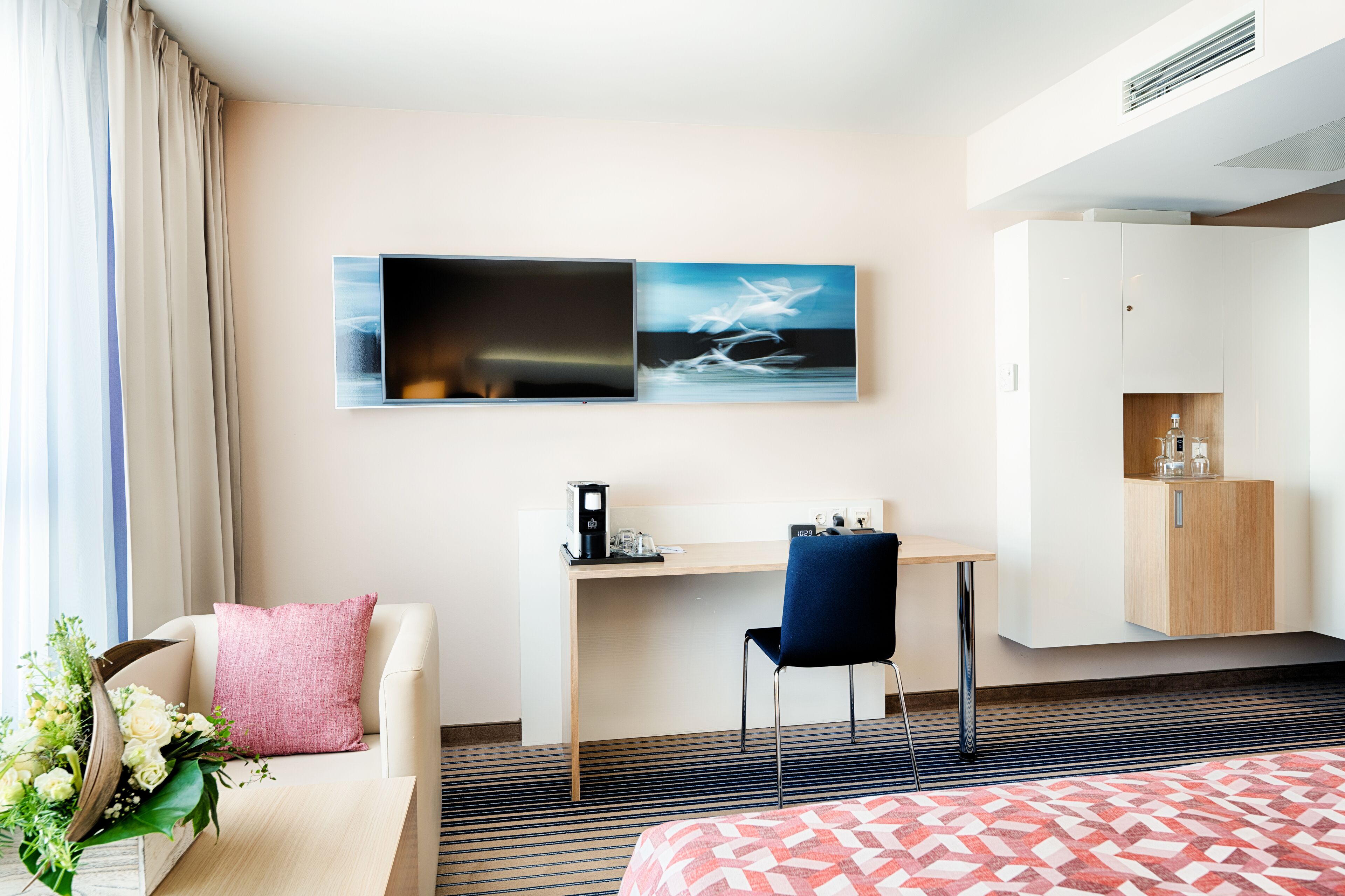 A hotel room with a bed, a desk, a chair, a sofa, a TV, and a cabinet.
