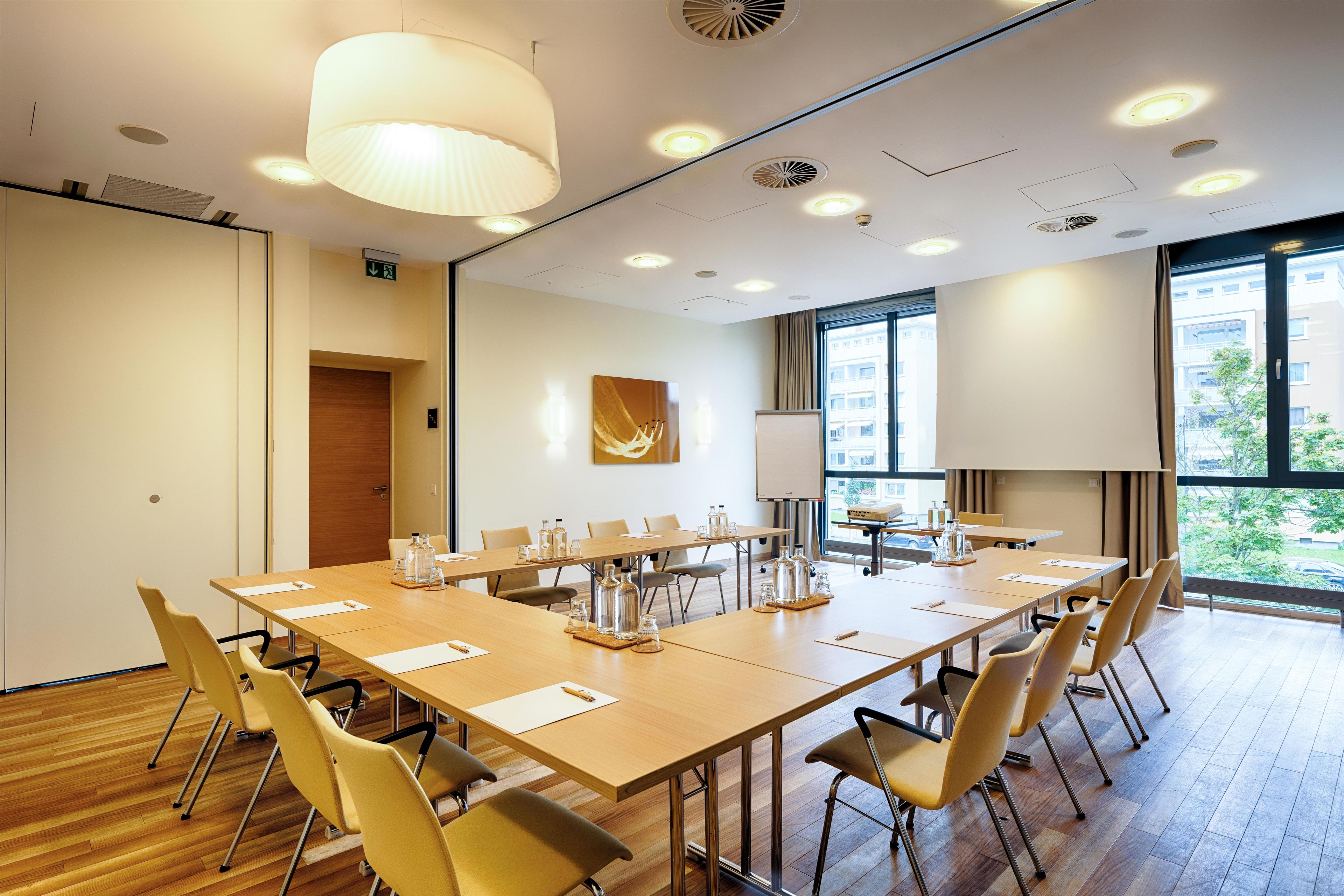 A conference room with a long table, chairs, a whiteboard, and a large window with a view of buildings.